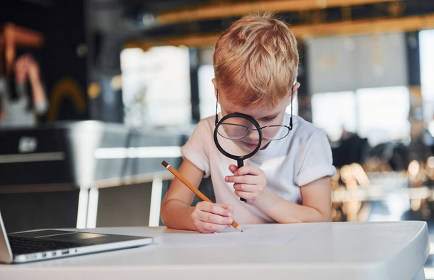 Smart child in casual clothes with laptop on table have fun with magnifying glass. - Fotoğraf, Görsel