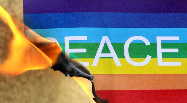Peace flag with rainbow colors burning with fire flame and golden background - Photo, image