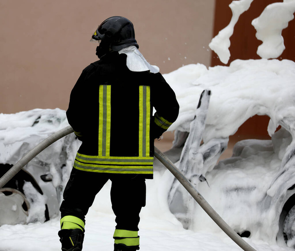 Mutiger Feuerwehrmann nach dem Löschen des brennenden Autos, das nun voll mit Löschschaum ist - Foto, Bild