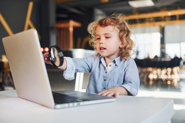 Smart child in casual clothes with laptop on table have fun with magnifying glass. - Foto, Bild