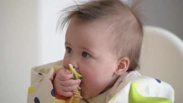 An infant 7-month caucasian girl is eating broccoli with bare hands. - Video