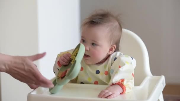 Baby girl is checking the dinner while sitting in a white highchair. - Video