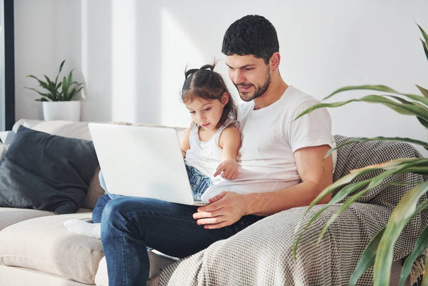 Szczęśliwy ojciec z córką spędzają wolny czas z laptopem w domu razem. - Zdjęcie, obraz