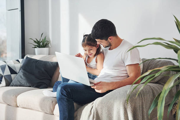 Happy father with his daughter spending free time with laptop at home together. - Foto, Imagen