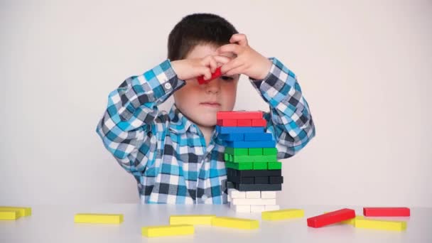 Ένα παιδί προσχολικής ηλικίας παίζει, χτίζει προσεκτικά έναν πύργο από πολύχρωμα ξύλινα μπλοκ - Πλάνα, βίντεο