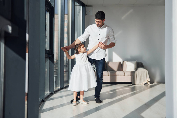 Happy father with his daughter in dress learning how to dance at home together. - Φωτογραφία, εικόνα