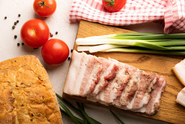 Board with pork fat, green onions, homemade bread and cherry tomatoes on a gray stone background. Salo. Delicious salty lard with pepper. Space for copy. Space for text. - Foto, Imagen