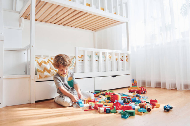 Cute little boy sitting and have fun indoors in the bedroom with plastic construction set. - Foto, Imagem