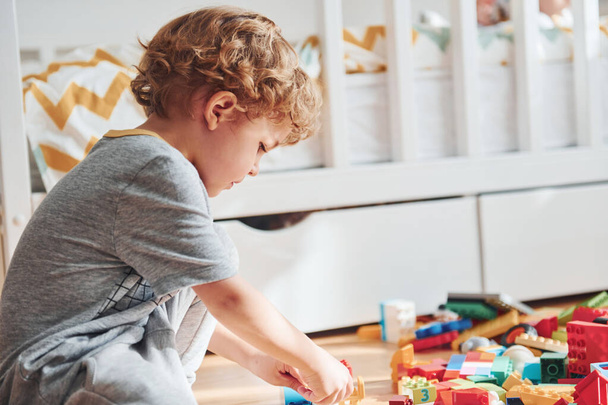 Cute little boy sitting and have fun indoors in the bedroom with plastic construction set. - 写真・画像