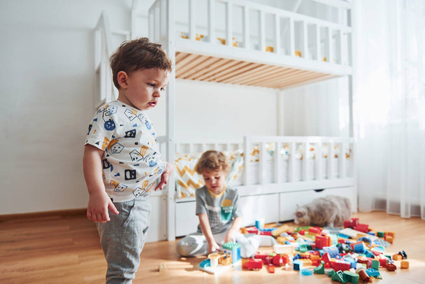 Two little boys have fun indoors in the bedroom with plastic construction set. - 写真・画像