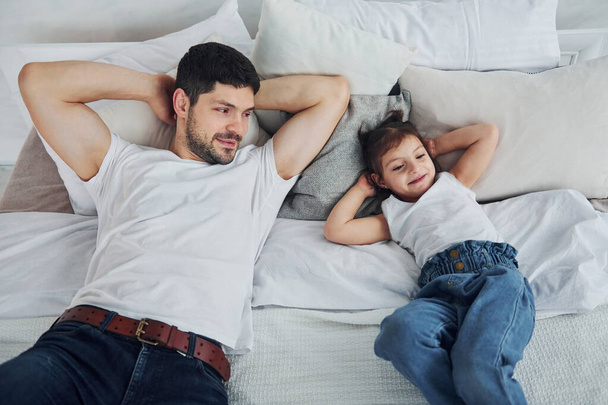 Happy father with his daughter spending free time at home together. Lying down on bed. - Foto, immagini
