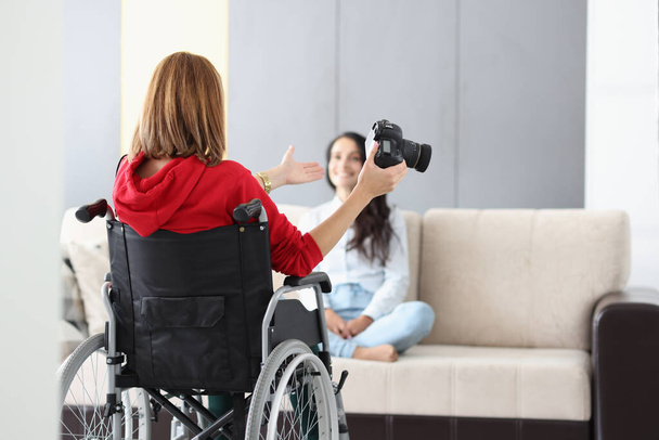 Professional photographer in wheelchair give advice on posing to model on sofa - Foto, Imagen