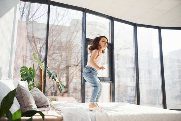 Cute little girl at home alone. Having fun by jumping on the bed. - Foto, afbeelding
