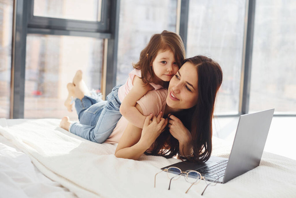 Young mother with her daughter spending weekend together in room and using laptop. - Foto, immagini