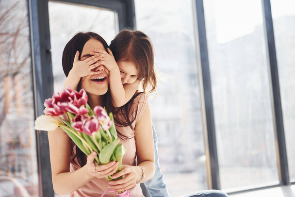 Covering eyes. Daughter congratulates mother with holiday and gives bouquet of flowers. - Фото, зображення