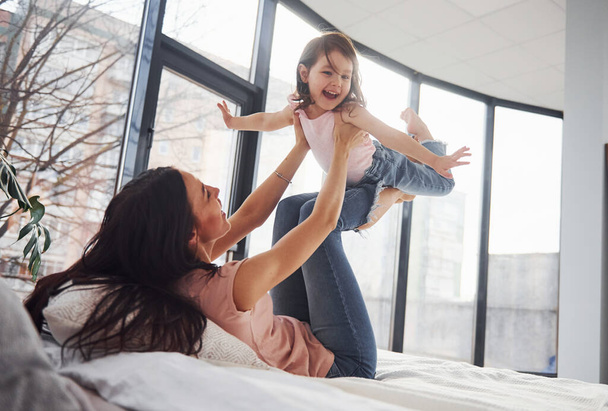 Young mother with her daughter spending weekend together on bed. - Foto, Bild