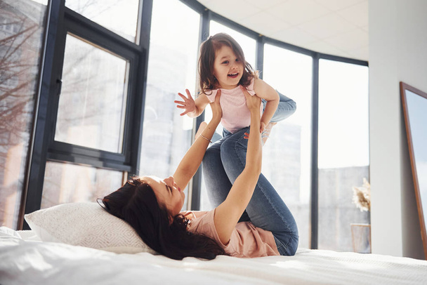 Young mother with her daughter have fun at weekend time together on bed. - Foto, afbeelding