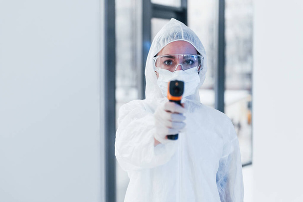 Holds infrared thermometer. Portrait of female doctor scientist in lab coat, defensive eyewear and mask. - Foto, imagen