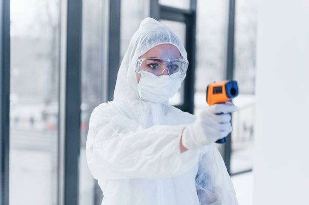 Holds infrared thermometer. Portrait of female doctor scientist in lab coat, defensive eyewear and mask. - Foto, immagini