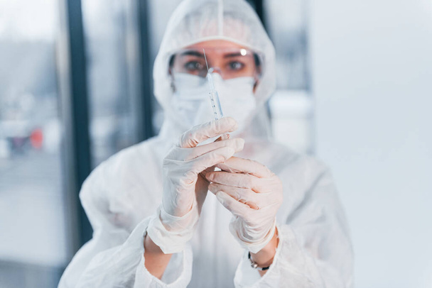 Holds syringe. Portrait of female doctor scientist in lab coat, defensive eyewear and mask. - Foto, Imagem
