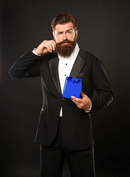 man in tuxedo bow tie formalwear with moustache on black background with gift box. boxing day - Zdjęcie, obraz