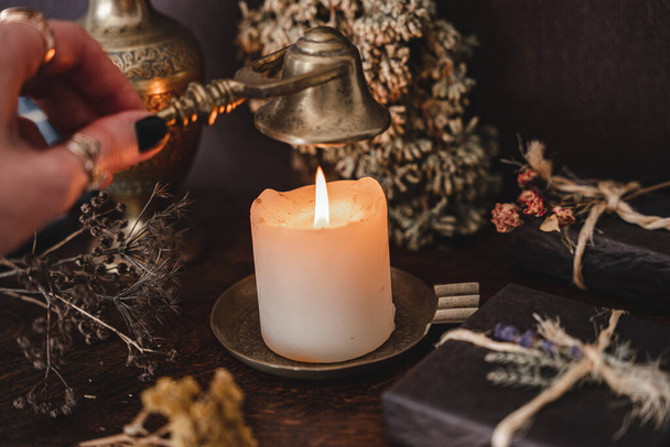 Wiccan witch putting out a white candle flame with antique brass gold colored wick snuffer. Casting a spell at a witch's altar - Zdjęcie, obraz