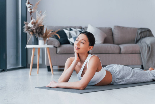 Lying down on the mat and taking a break. Young woman with slim body shape in sportswear have fitness day indoors at home. - Foto, Bild