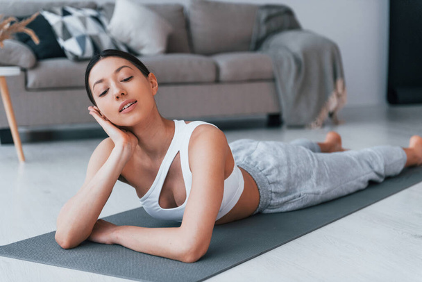 Lying down on the mat and taking a break. Young woman with slim body shape in sportswear have fitness day indoors at home. - Fotoğraf, Görsel