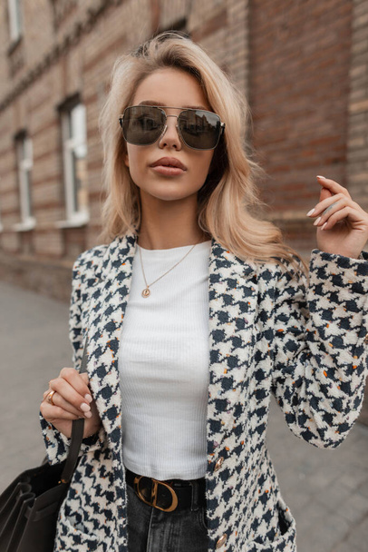 Fashion beautiful blonde girl in fashionable casual clothes with glasses and a bag walks in the city - Foto, immagini