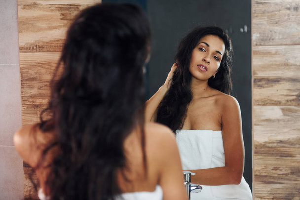 Beautiful young woman standing in bathroom near the mirror. - Фото, зображення