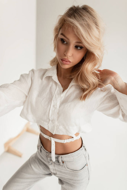 Glamorous beautiful stylish blonde woman in fashionable clothes with a shirt and jeans makes a selfie photo in the studio - Photo, Image