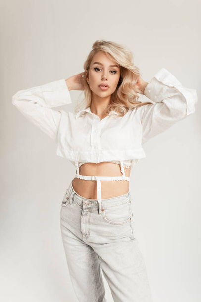 Fashionable beautiful stylish elegant girl model in a fashionable white shirt and stylish jeans with a high waist in the studio on a white background - Photo, Image