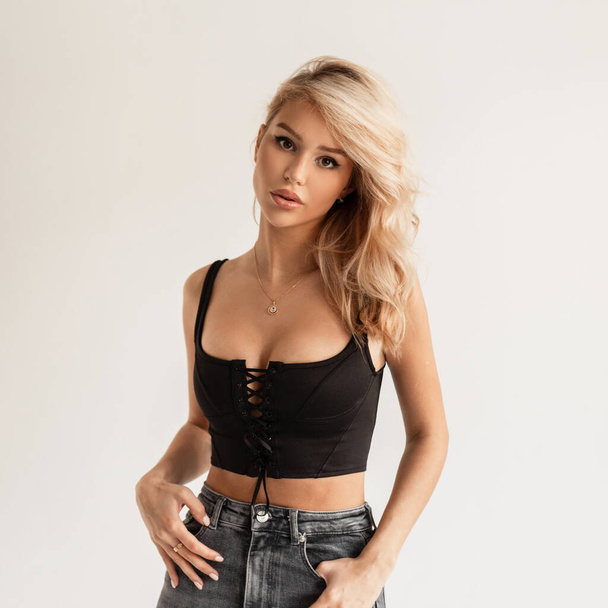 Sexy beautiful glamorous young blonde woman in a black bustier top and High waisted jeans posing in the studio on a white background - Fotoğraf, Görsel