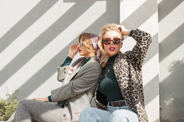 Zwei Modemädchen in stylischer Kleidung sitzen auf der Straße - Foto, Bild