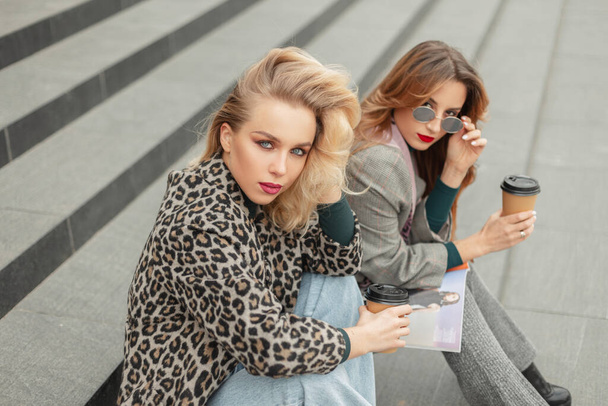 Стильна молода блондинка з подругою в модному одязі, сидячи в місті
 - Фото, зображення