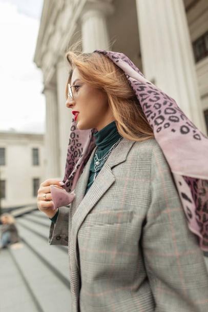 Mujer de moda bonita en traje de moda con estilo con bufanda en la cabeza paseos por la ciudad. Ropa urbana de estilo femenino - Foto, Imagen