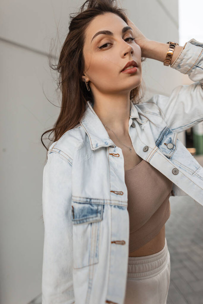 Urban stylish young girl with a beautiful face in a fashionable denim jacket walks in the city - Fotó, kép