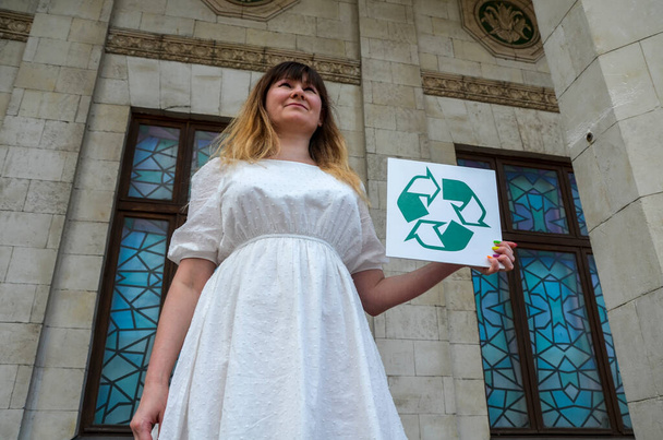Эколог-активистка держит белую доску с логотипом утилизации. Концепция переработки, повторного использования отходов, охраны окружающей среды и экологии - Фото, изображение