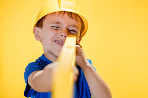The preschooler holds a construction level in his hands, dreams of becoming a builder. - Foto, Imagen