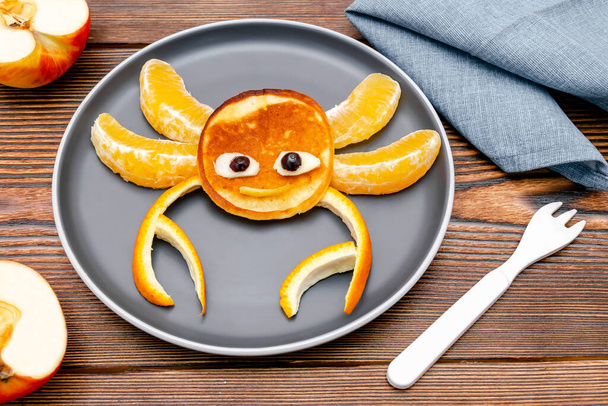 Funny crab face shape snack from pancake, orange,apples on plate. Cute kids childrens baby's sweet dessert, healthy breakfast,lunch, food art on wooden background,top view. - Zdjęcie, obraz