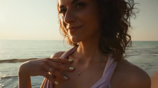 Face close up: Beautiful young woman in long dress looking at you against sunset sea background - Materiaali, video
