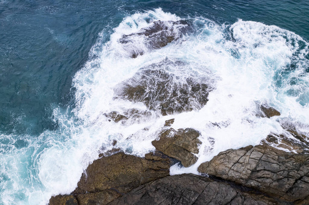 Aerial view Drone camera top down of seashore rocks in a blue ocean Turquoise sea surface Amazing sea waves crashing on rocks seascape. High quality image of sea waves in Phuket Thailand - Foto, Imagen