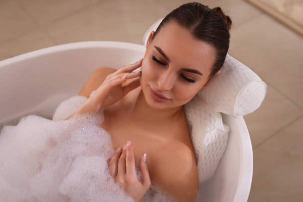 Young woman using pillow while enjoying bubble bath indoors - Photo, Image