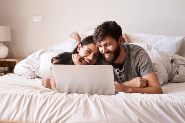 Joillakin on vain se erityinen yhteys. Laukaus onnellinen nuori pari käyttää kannettavaa tietokonetta rentoutuessaan sängyssä kotona. - Valokuva, kuva