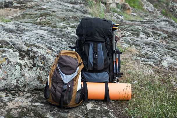 Backpacks with trekking poles and camping mat on rocky hill - 写真・画像
