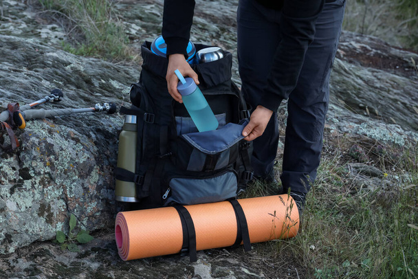 Hiker putting bottle of water into backpack on rocky hill, closeup - Foto, immagini