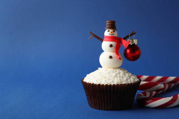 Tasty cupcake with snowman figure and Christmas bauble on blue background, space for text - Fotografie, Obrázek