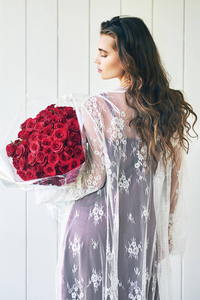 Flowers brings the lady out of you. Rearview shot of a beautiful young woman standing with her eyes closed while holding a bouquet of roses outside. - Photo, Image