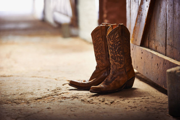 Another day done. Shot of a pair of cowboy boots in a barn. - Photo, Image