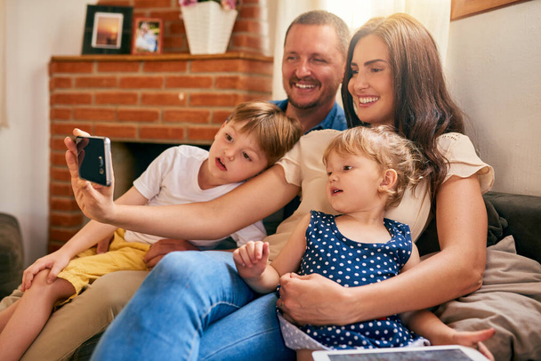 Tärkeimmät muistot ovat ne, joilla on perhe. Kuvattu onnellinen nuori perhe ottaa selfien yhdessä sohvalla kotona. - Valokuva, kuva